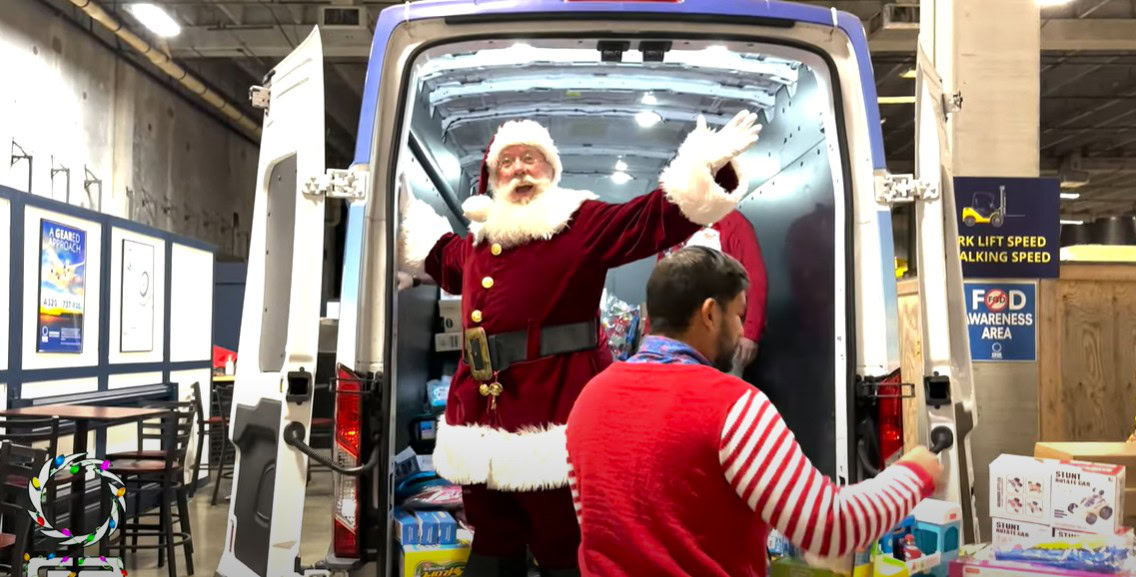 Santa delivering gifts at community event in a warehouse setting.